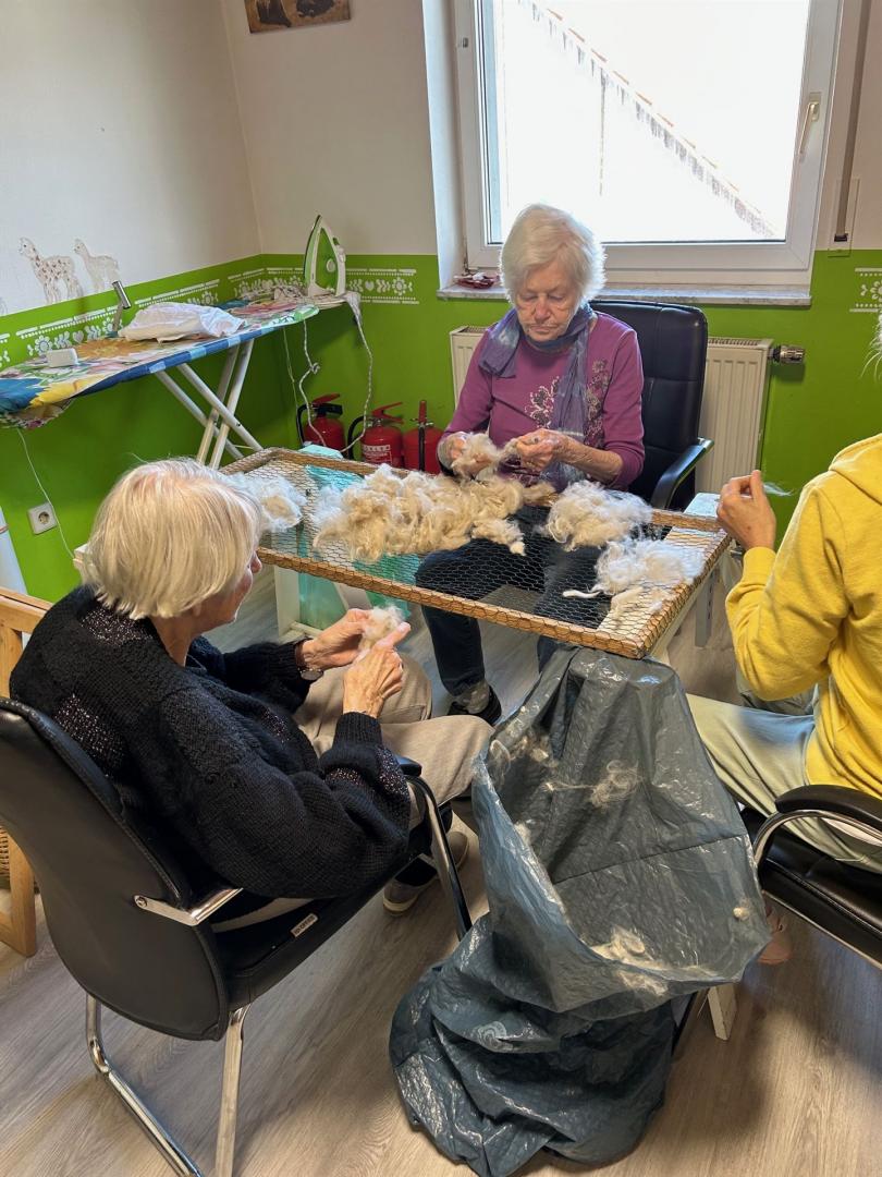 Drei Personen arbeiten gemeinsam an einem gefüllten Korb mit Flaummaterial, was auf eine Bastel- oder Wollverarbeitung hindeutet.
